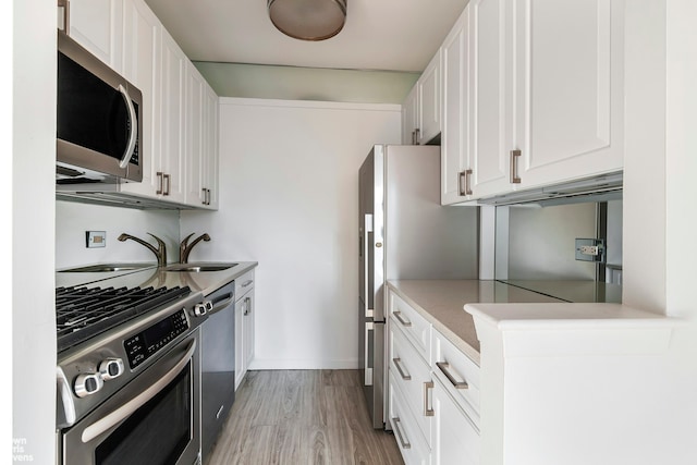 kitchen with stainless steel appliances, light countertops, light wood-style flooring, white cabinets, and a sink