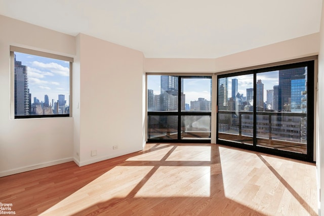 empty room with a view of city, baseboards, and wood finished floors