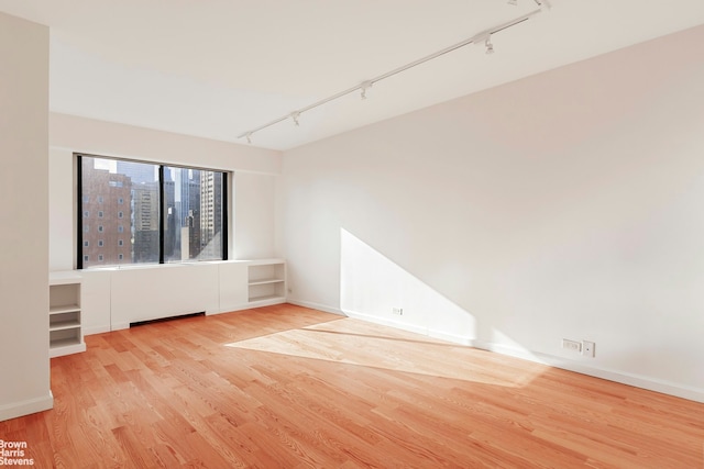 spare room with light wood finished floors, baseboards, a city view, and track lighting