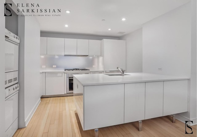 kitchen with light countertops, a peninsula, a sink, and white cabinets