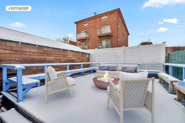 snow covered patio featuring an outdoor living space with a fire pit and fence