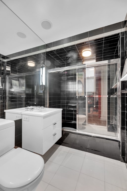 full bathroom featuring toilet, combined bath / shower with glass door, tile walls, and vanity