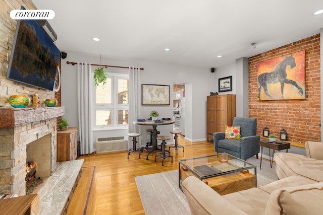 living room with an AC wall unit, a large fireplace, and light hardwood / wood-style floors