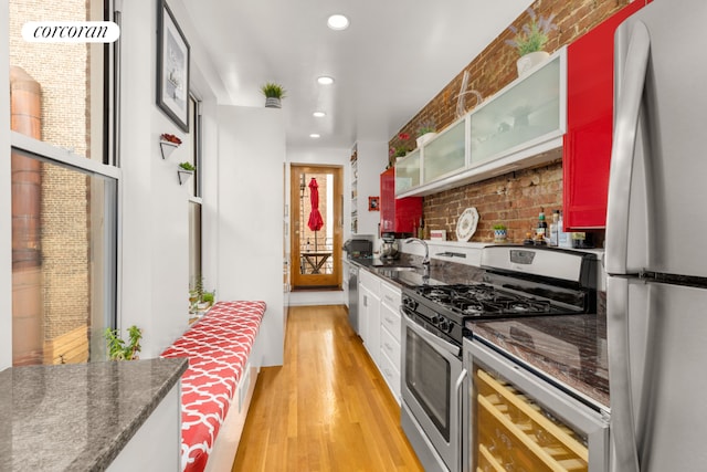 kitchen with sink, dark stone countertops, stainless steel appliances, and light hardwood / wood-style floors