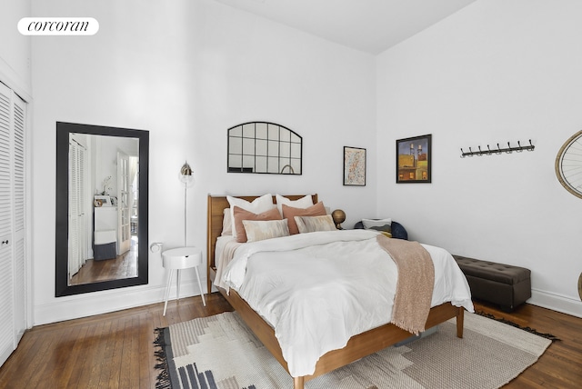 bedroom with baseboards, visible vents, wood finished floors, a high ceiling, and a closet