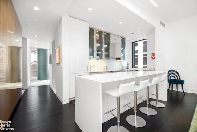 kitchen featuring a breakfast bar area, white cabinets, dark hardwood / wood-style flooring, decorative backsplash, and kitchen peninsula