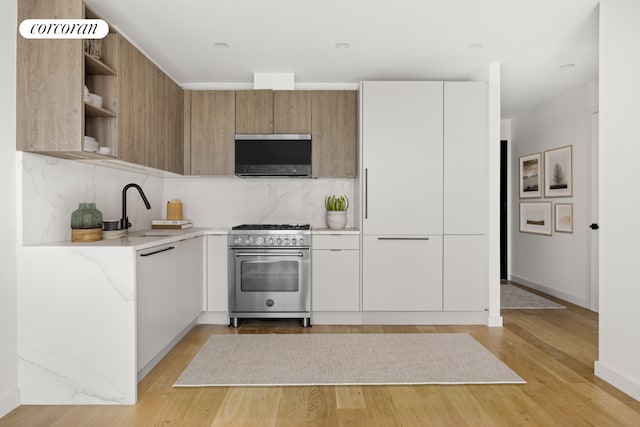 kitchen with white cabinetry, light wood-type flooring, sink, tasteful backsplash, and high end stove