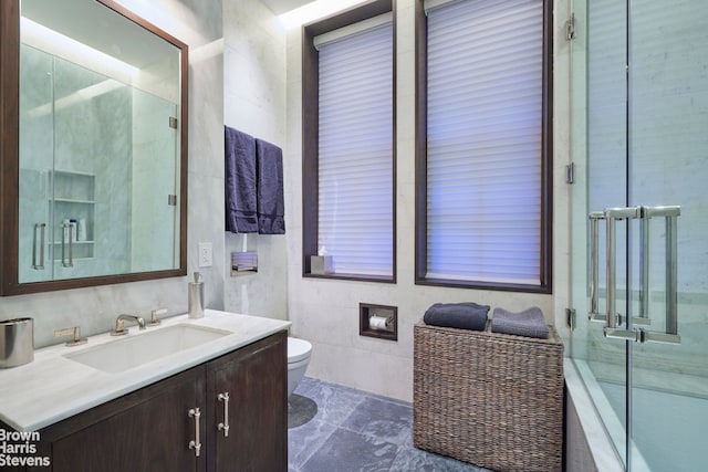 full bathroom featuring tile walls, a shower with door, vanity, and toilet