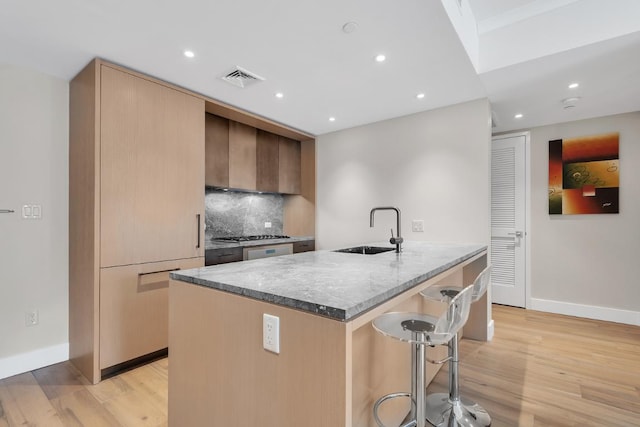 kitchen with sink, a kitchen breakfast bar, decorative backsplash, light hardwood / wood-style floors, and a center island with sink