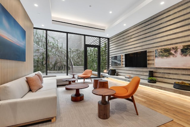 living room with expansive windows, a raised ceiling, and light wood-type flooring