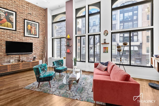 living area featuring baseboards, brick wall, wood finished floors, and a towering ceiling