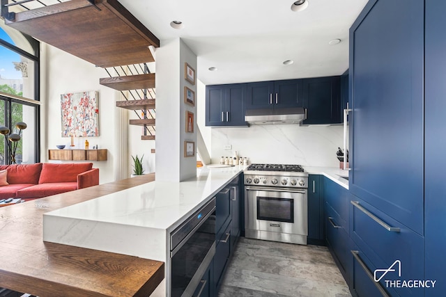 kitchen with decorative backsplash, appliances with stainless steel finishes, a peninsula, blue cabinets, and under cabinet range hood