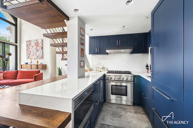 kitchen featuring stainless steel appliances, blue cabinetry, under cabinet range hood, a peninsula, and light wood-style floors