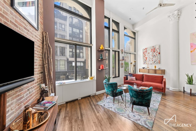 living room with wood finished floors, baseboards, a ceiling fan, a towering ceiling, and brick wall
