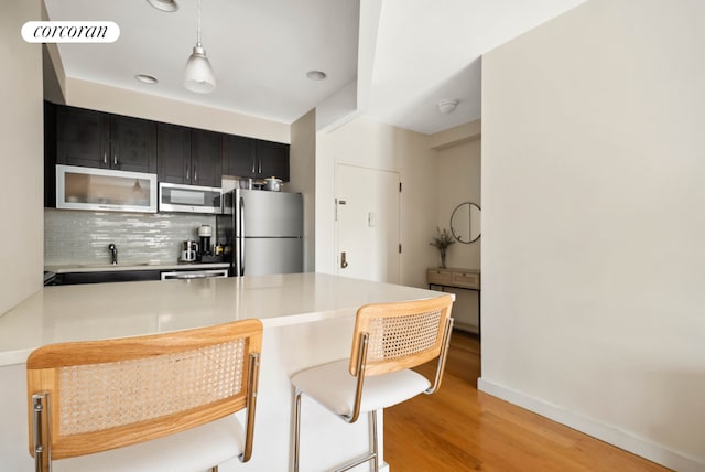 kitchen featuring a peninsula, light countertops, dark cabinetry, appliances with stainless steel finishes, and decorative backsplash