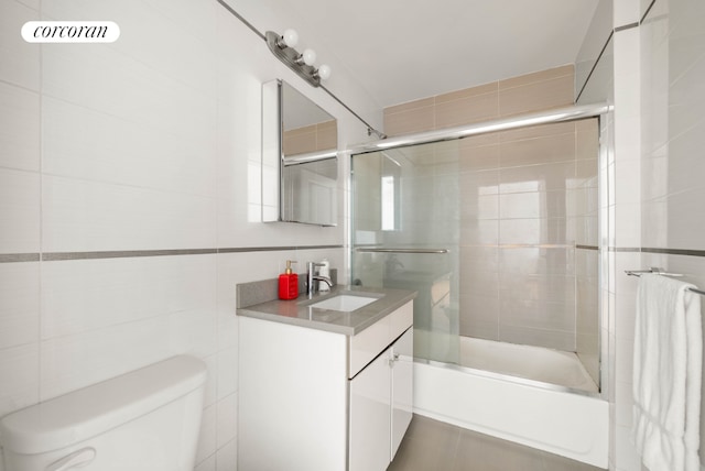 bathroom featuring toilet, bath / shower combo with glass door, tile walls, and vanity