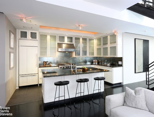 kitchen featuring an island with sink, white cabinetry, paneled fridge, and tasteful backsplash