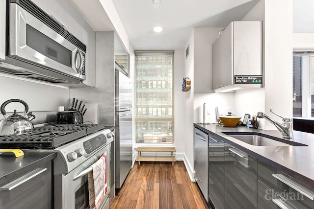 kitchen featuring dark wood-style flooring, dark countertops, a sink, stainless steel appliances, and modern cabinets