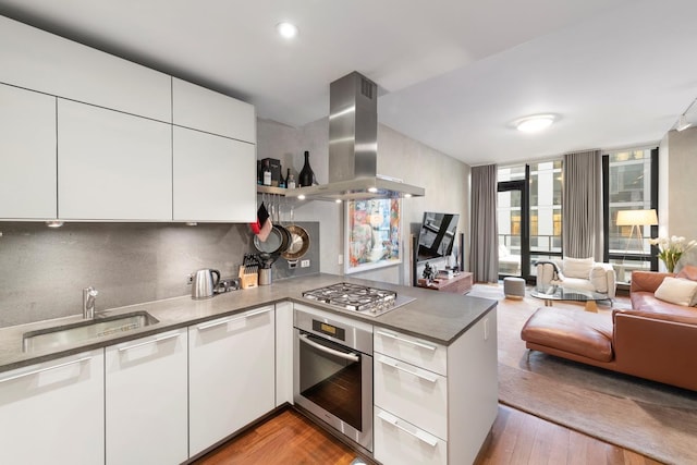 kitchen with island exhaust hood, appliances with stainless steel finishes, open floor plan, a sink, and a peninsula