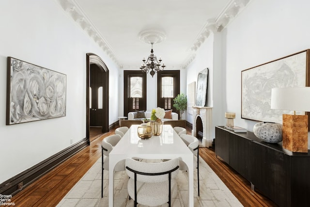 dining room featuring baseboards, arched walkways, wood finished floors, crown molding, and a notable chandelier