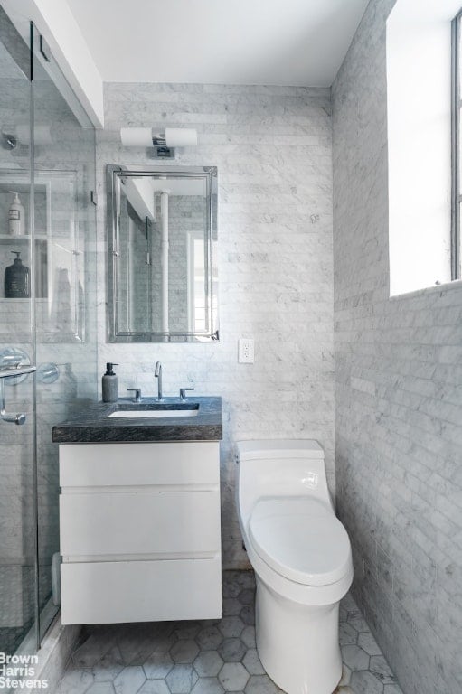 bathroom with vanity, toilet, an enclosed shower, and tile walls