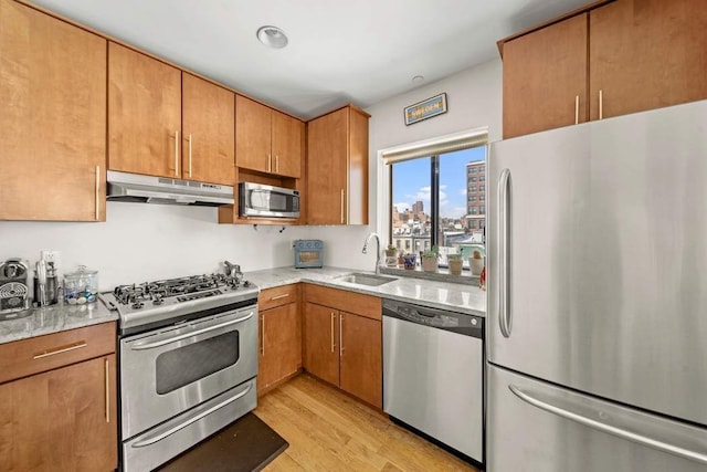kitchen with a sink, brown cabinets, stainless steel appliances, light wood-style flooring, and under cabinet range hood