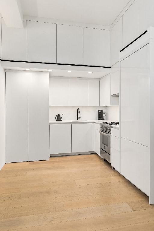 kitchen featuring high end range, sink, light hardwood / wood-style flooring, and white cabinets