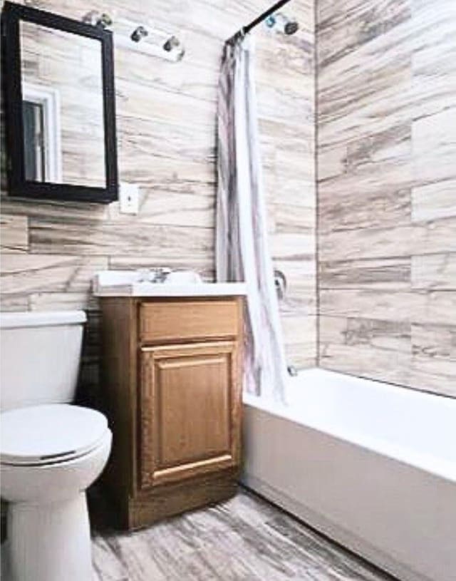 bathroom with toilet, shower / bathtub combination with curtain, wood finished floors, and vanity
