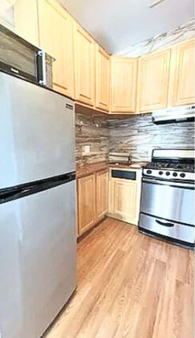 kitchen featuring decorative backsplash, light wood-style floors, stainless steel appliances, light brown cabinetry, and ventilation hood
