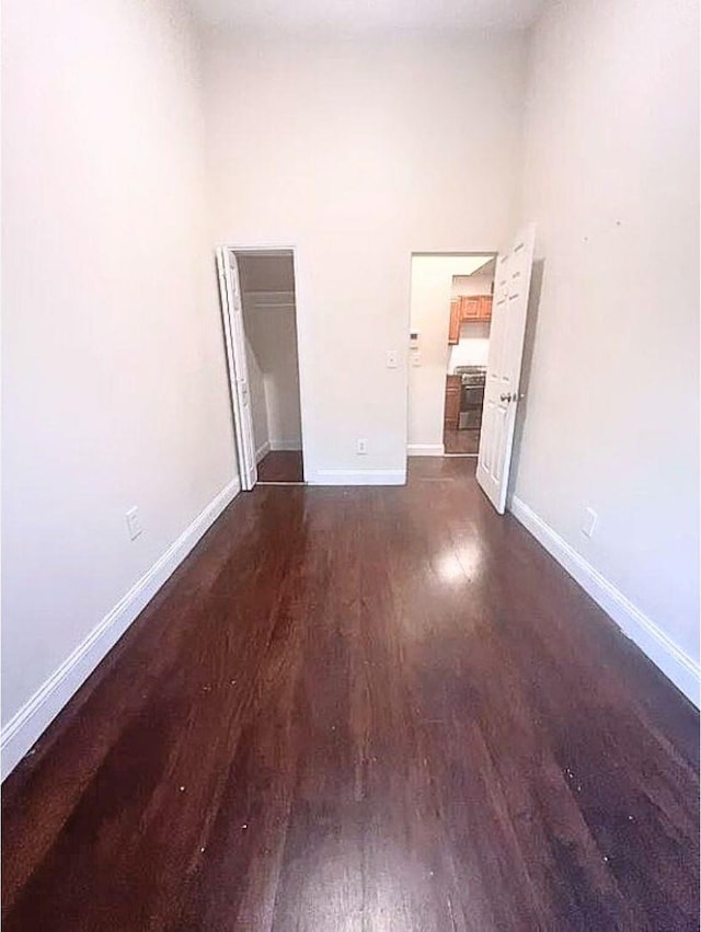 empty room with a high ceiling, dark wood finished floors, and baseboards