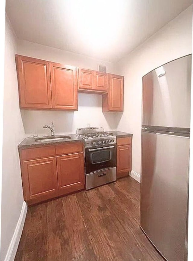 kitchen featuring dark wood finished floors, baseboards, stainless steel appliances, and a sink