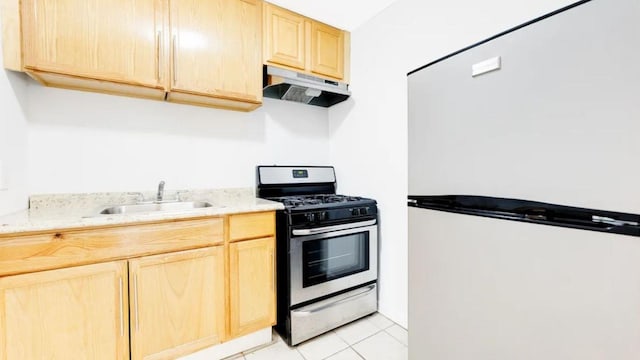 kitchen with a sink, stainless steel range with gas stovetop, under cabinet range hood, white fridge, and light brown cabinetry