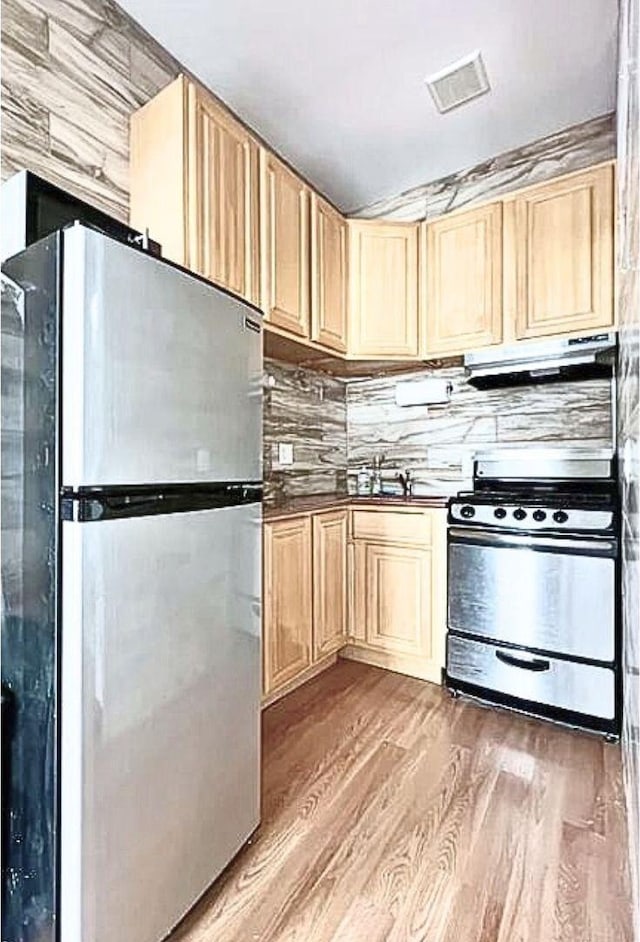 kitchen with decorative backsplash, light wood-style floors, light brown cabinets, stainless steel appliances, and under cabinet range hood
