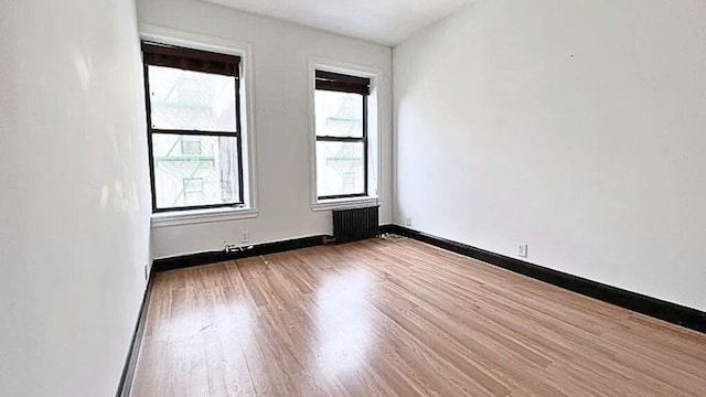 unfurnished room with baseboards, radiator, and wood finished floors