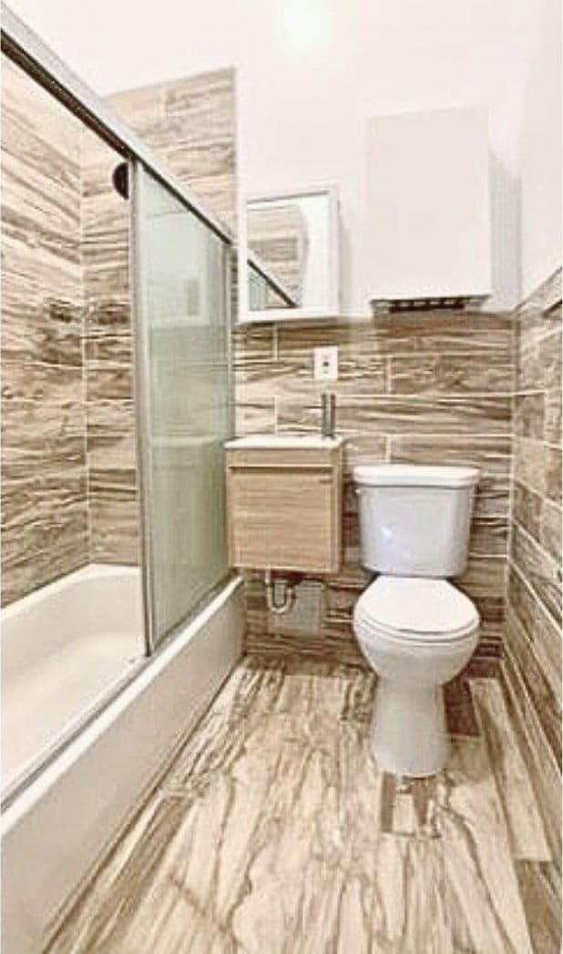 bathroom with enclosed tub / shower combo, toilet, tile walls, vanity, and marble finish floor