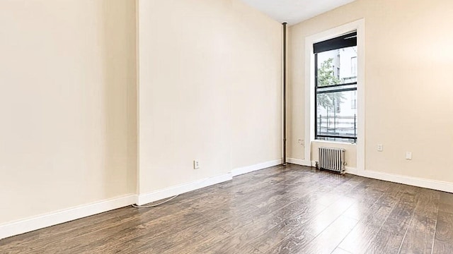 spare room featuring dark wood finished floors, radiator heating unit, and baseboards
