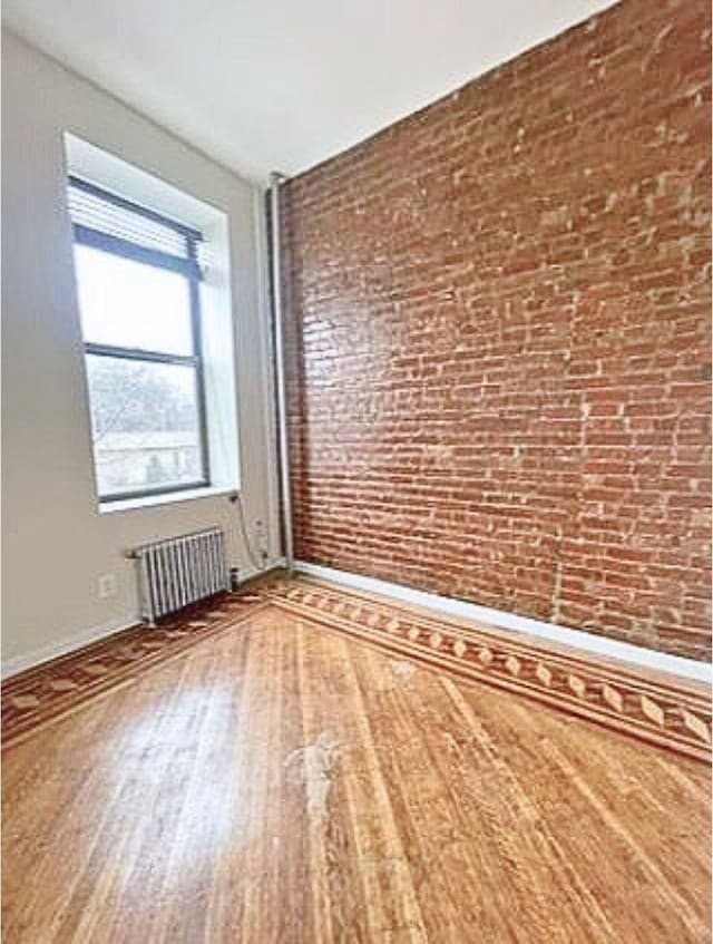 spare room featuring wood finished floors, baseboards, and radiator