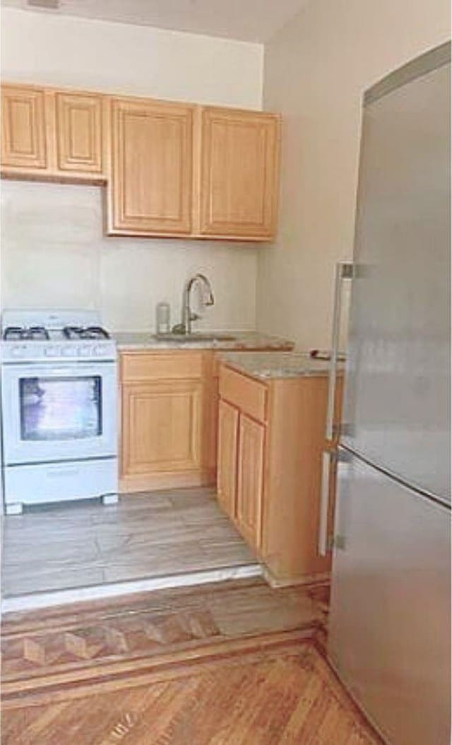 kitchen featuring a sink, light brown cabinets, white range with gas stovetop, stainless steel fridge, and light countertops