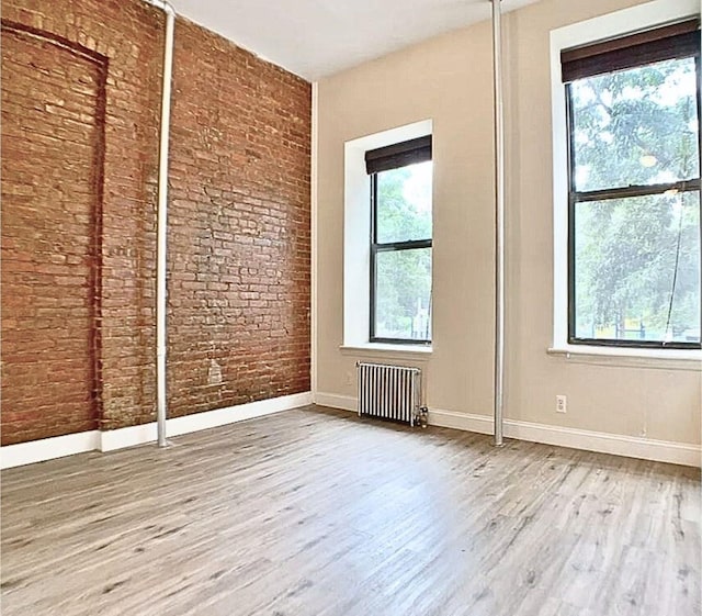 unfurnished bedroom with baseboards, radiator heating unit, wood finished floors, and brick wall