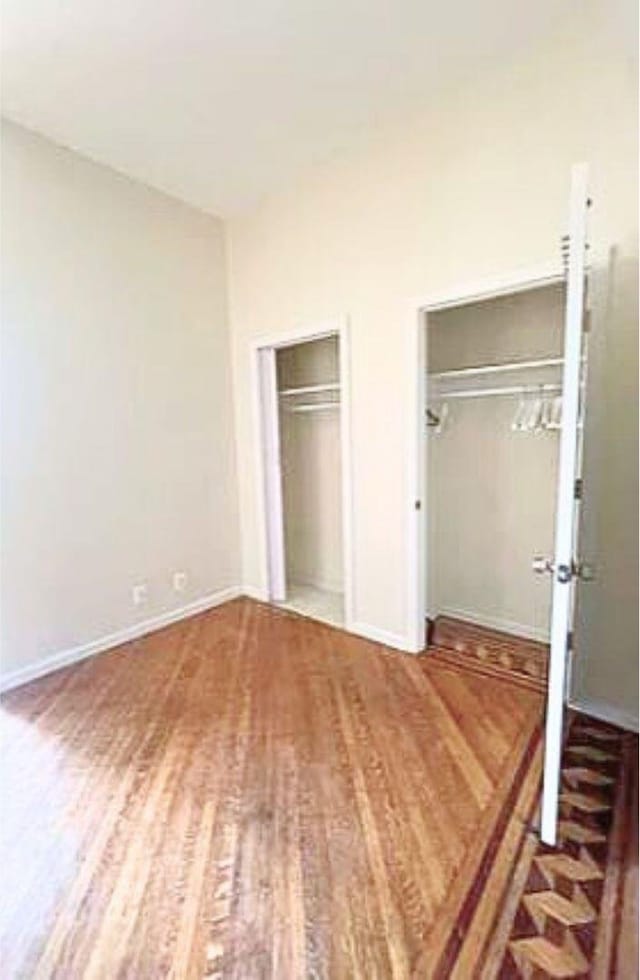 unfurnished bedroom with wood finished floors, multiple closets, and baseboards
