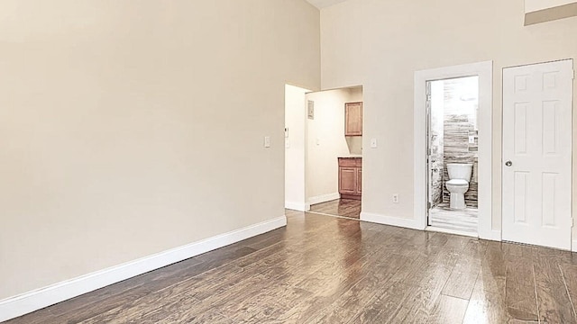unfurnished bedroom with dark wood-style floors, a high ceiling, baseboards, and ensuite bath