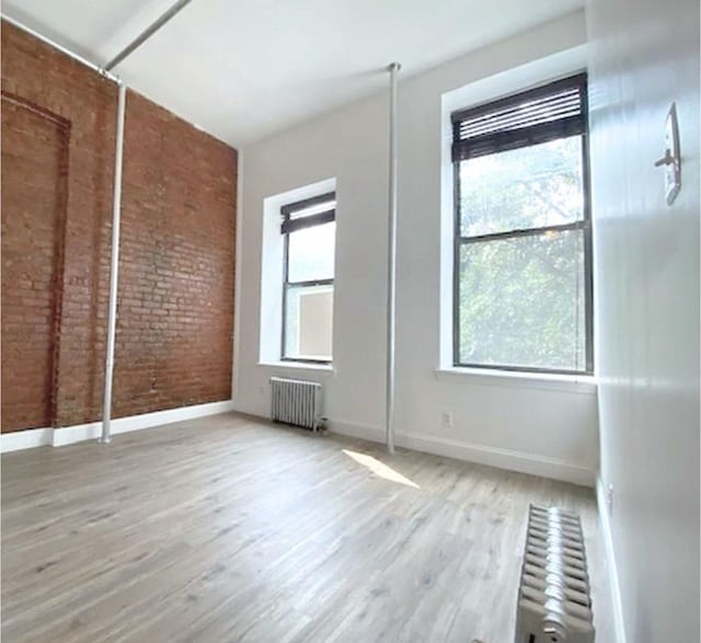 unfurnished bedroom with brick wall, radiator heating unit, wood finished floors, and baseboards