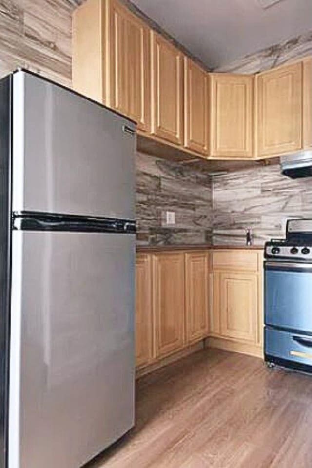 kitchen featuring range with gas stovetop, decorative backsplash, light brown cabinetry, light wood-style flooring, and freestanding refrigerator
