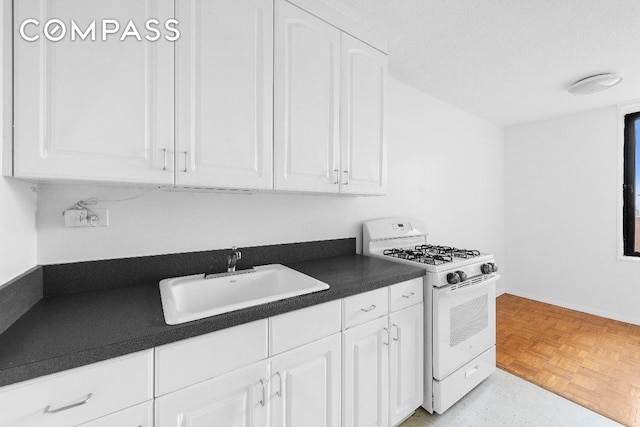 kitchen with dark countertops, a sink, white cabinetry, and white range with gas stovetop