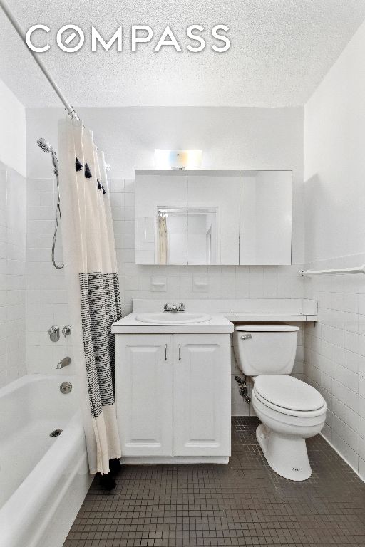 bathroom with a textured ceiling, tile patterned flooring, vanity, tile walls, and shower / bath combo