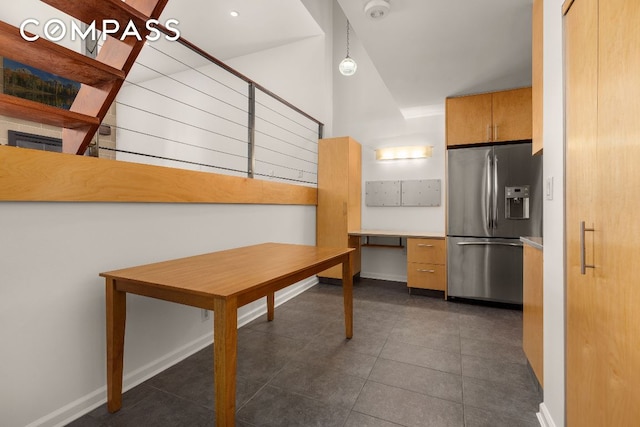 kitchen with stainless steel fridge, built in desk, hanging light fixtures, and dark tile patterned floors