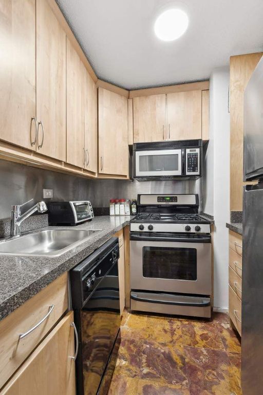 kitchen with light brown cabinetry, sink, stainless steel appliances, and dark stone counters