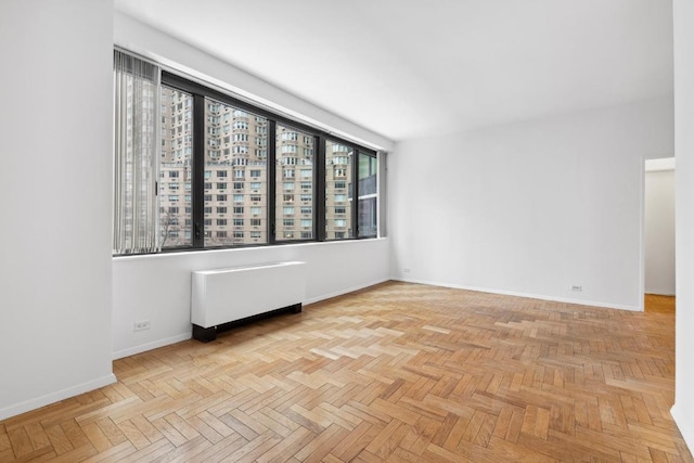 unfurnished room with radiator heating unit and light parquet floors