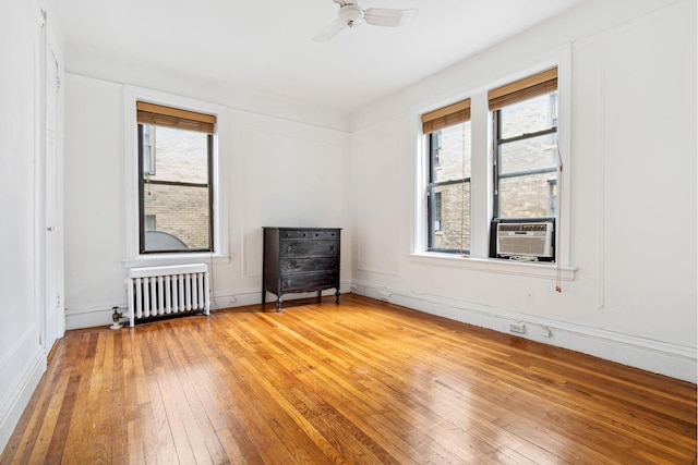empty room featuring radiator heating unit, cooling unit, light wood-type flooring, and a ceiling fan