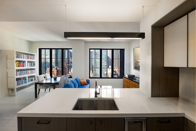 kitchen with dark brown cabinetry, open floor plan, light countertops, wood finished floors, and a sink